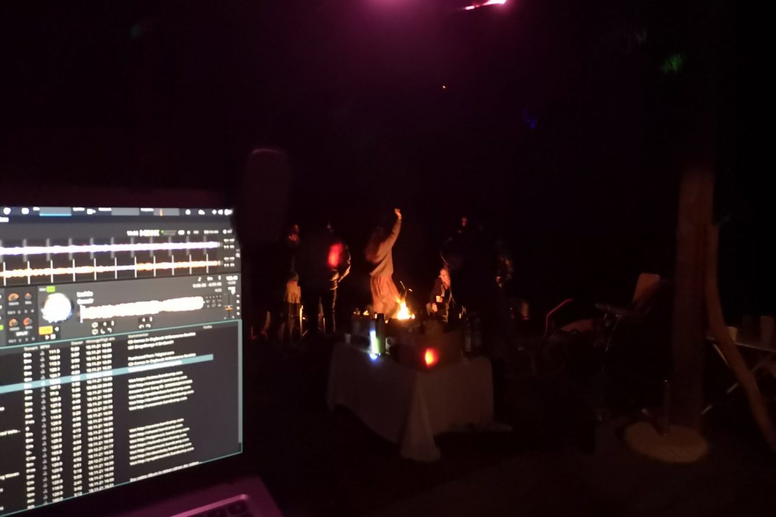 Menschen feiern in der Nacht bei einem Lagerfeuer aus der Sicht des DJs hinter seinem Laptop